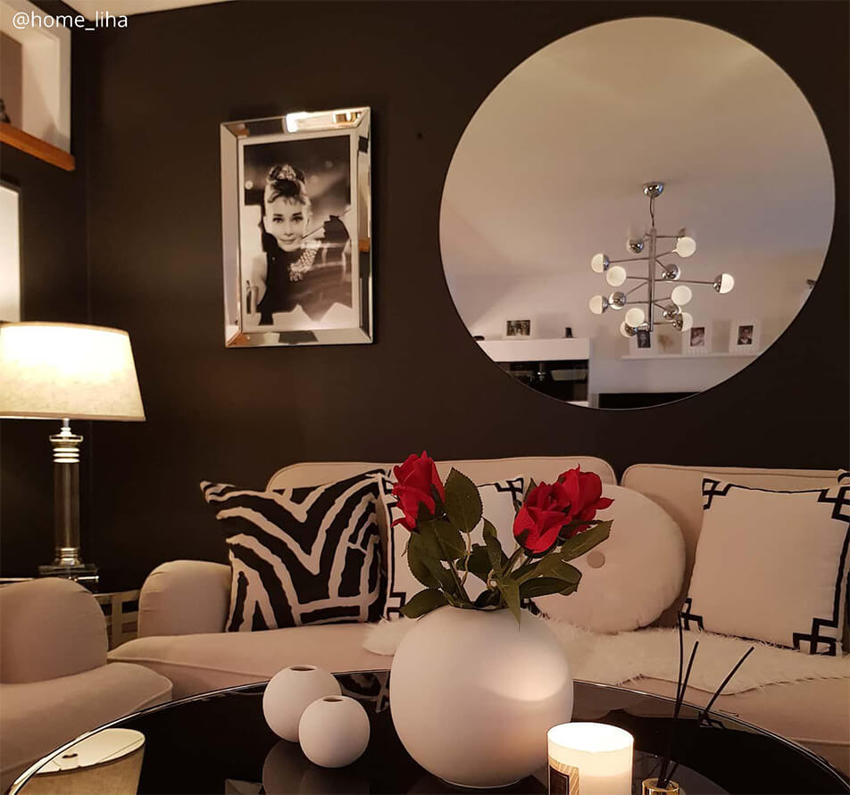 Vardagsrum med mörk väggfärg, vit soffa och stor, rund spegel